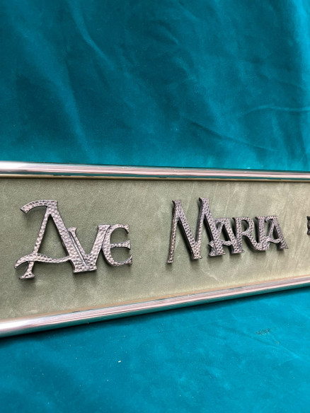 Cartel Ave María con letras en bronce y terciopelo verde de fondo.