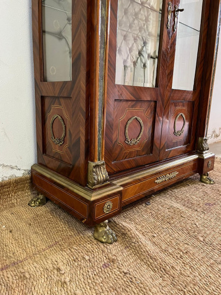 Vitrina estilo imperio con adornos en bronce, cristales biselados y capitoné.