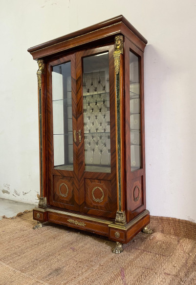 Vitrina estilo imperio con adornos en bronce, cristales biselados y capitoné.