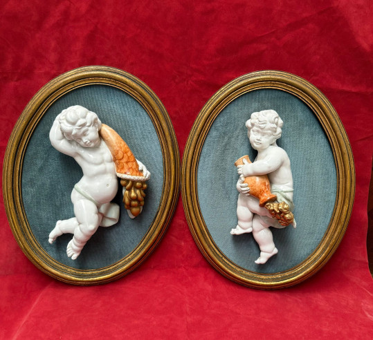 Pareja de ángeles en porcelanas sobre marco ovalado tapizado.